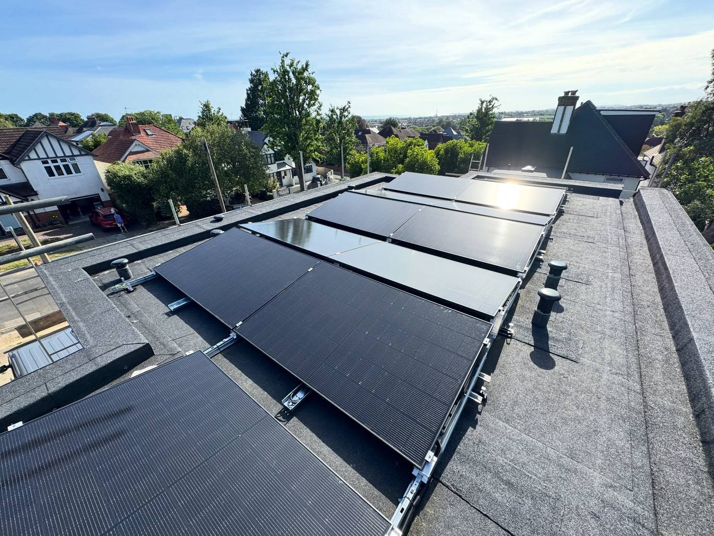Flat-roof solar PV array with surrounding houses and trees in the background